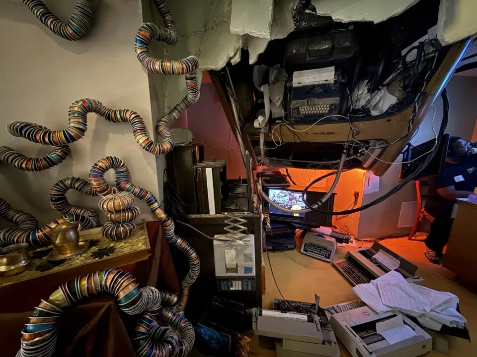 Immersive office scene with sculptural forms and typewriters lit in orange at Ministry of Awe